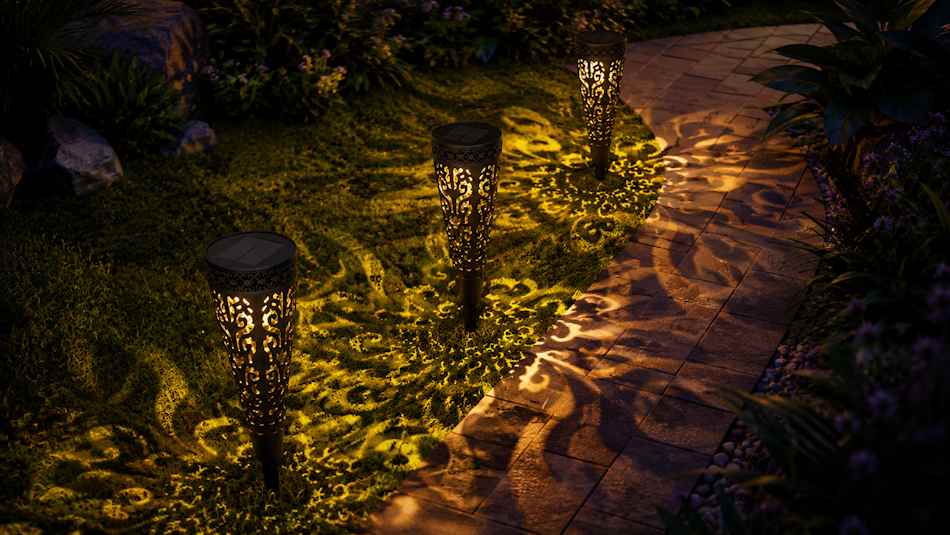 Zapichovacia solárna lampa Garden of Eden 13011 – dve lampy pri záhradnom chodníku v noci, ornamentálne tienidlové vzory na tráve a dlažbe, teplé zlaté svetlo